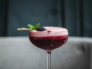 Cocktail in a glass decorated with berries and mint.