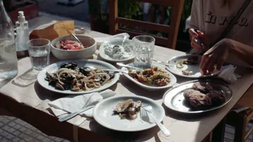 Table with Mediterranean food dishes under sunlight.