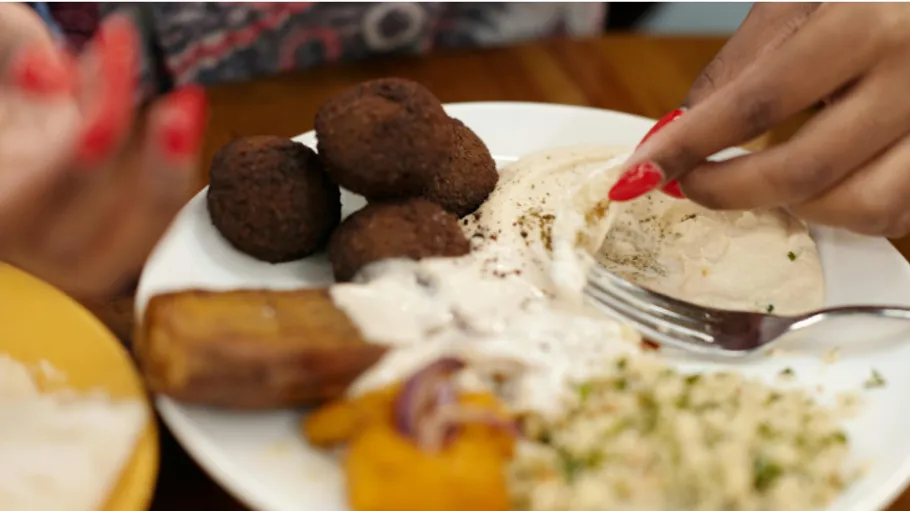 Schaufelt Essen mit der Hand auf einen Teller mit Hummus, Falafel, Salat.