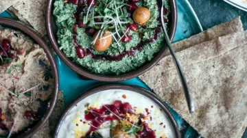 Mediterranean dips with garnishes and flatbread on a plate.