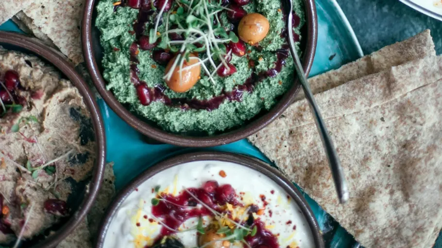 Mediterranean dips with garnishes and flatbread on a plate.