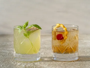 Zwei Cocktails stehen auf einer Holzoberfläche, einer grün, einer braun.
