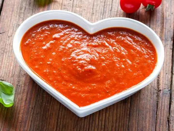Tomatensauce in herzförmiger Schüssel auf Holzuntergrund.