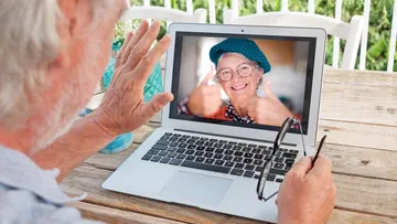 Elderly man video calling woman on laptop.