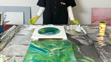 Person creating green abstract art on table.