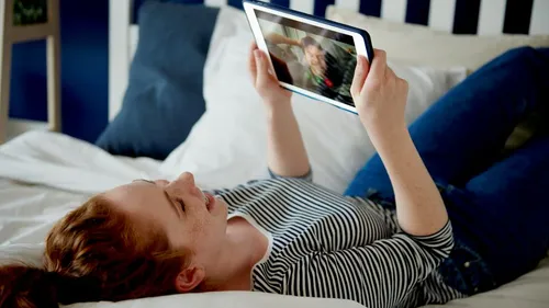 Woman video chatting on tablet in bed.