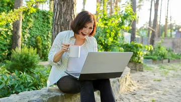 Woman with laptop and coffee in garden.