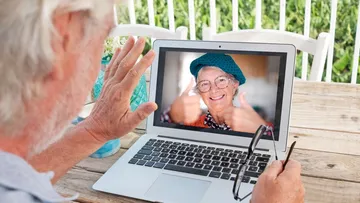 Elderly man video chatting with smiling woman on laptop.