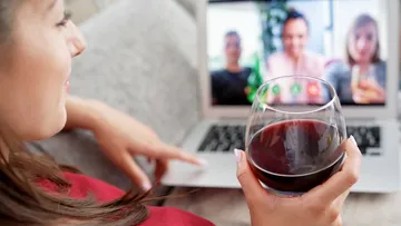 Frau hält ein Weinglas während eines Videoanrufs auf dem Laptop in der Hand.