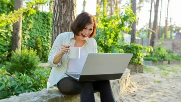 Frau benutzt Laptop und trinkt Kaffee im Freien.