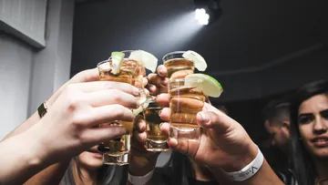 People clinking tequila shots with limes.