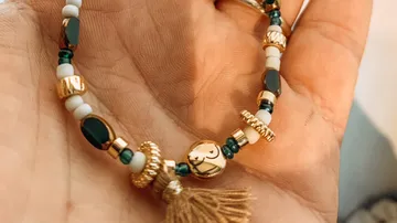 Hand holding bracelet with beads and tassel.