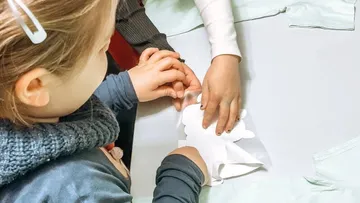 Kinder basteln mit Papierausschnitten.