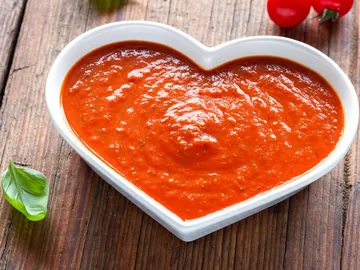 Herzförmige Schüssel mit roter Sauce auf Holzoberfläche.