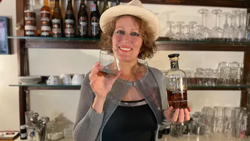 Frau hält Whiskyflasche und Glas, Bar-Hintergrund.