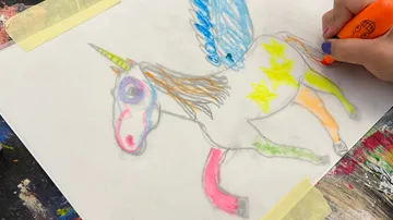 Person coloring a unicorn drawing on paper.