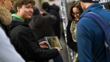 Person holding tablet, showing group outdoors.