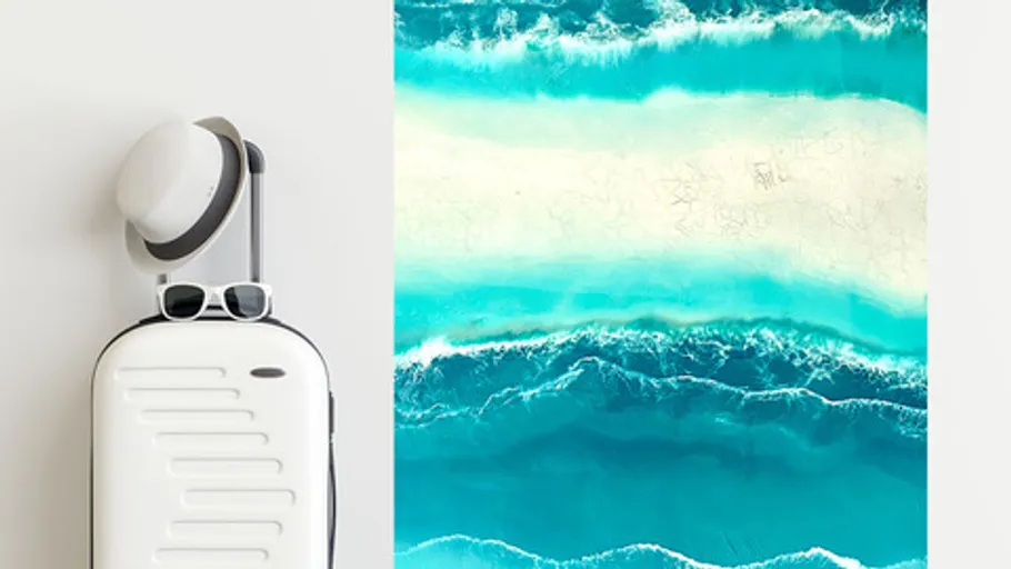 White suitcase with hat and sunglasses, ocean waves painting.