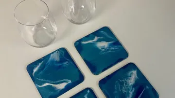 Zwei durchsichtige Gläser neben blauen Untersetzern mit Wolkenmuster.