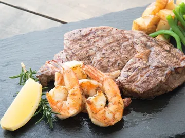 Steak und Garnelen auf einem schwarzen Teller serviert.