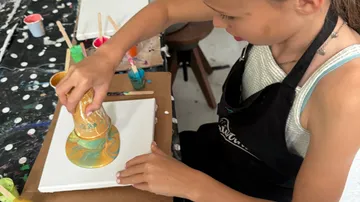 Child pours paint on canvas in studio.