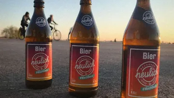 Drei Bierflaschen auf dem Bürgersteig, Radfahrer im Hintergrund.
