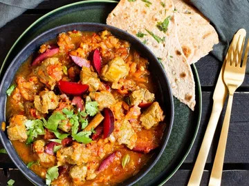 Stew with meat, vegetables and pita bread on a table.