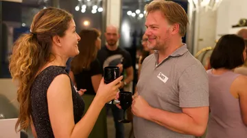 Two people holding drinks and talking at a social event.