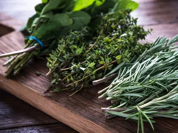 Fresh herbs lie on a wooden board.