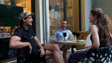 Drei Personen sitzen draußen an einem Cafétisch.