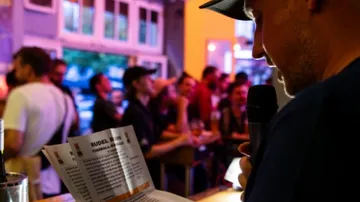 Person reading from paper in crowded bar.