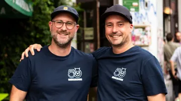 Two smiling men wearing matching blue T-shirts outdoors.
