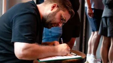Man signing papers in a busy lobby.