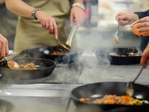 Several hands cook in steaming pans in a kitchen.