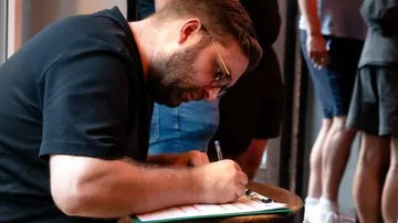 Man writing on clipboard in crowded room.