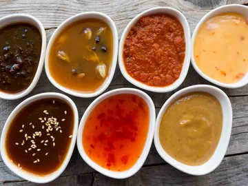 Eight bowls of various sauces on a wooden surface.