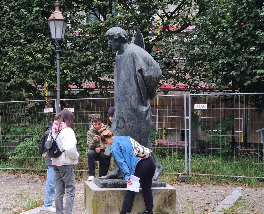 People examining metal statue in park.