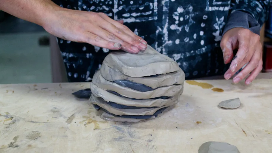 Hands shaping layered clay on wooden table.