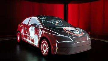 Car illuminated with geometric light projections in dark room.