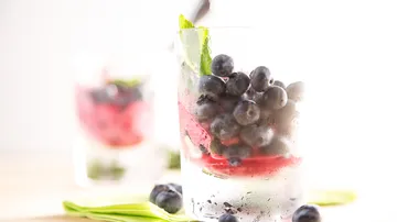 Glas mit Blaubeeren und Minze, heller Hintergrund.