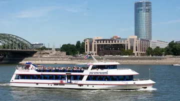 Ein Ausflugsschiff fährt auf dem Rhein unter einer Brücke.