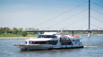 An excursion boat sails on the Rhine under a bridge.