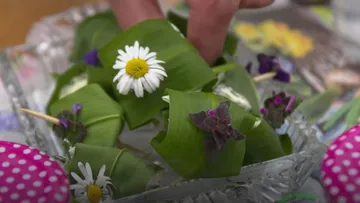 Platziert mit der Hand eine Blume auf eine mit Blättern umwickelte Schale.