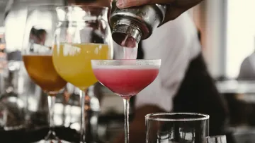 Bartender pouring pink cocktail into glass.