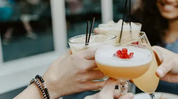 Hands holding cocktails in a toast outside.