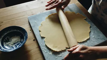 Hands rolling dough with rolling pin on table.