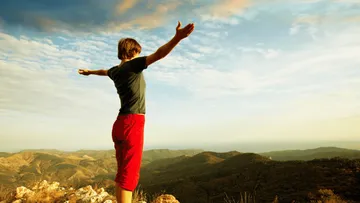 Person mit offenen Armen auf einem Berg, mit Blick auf die Landschaft.