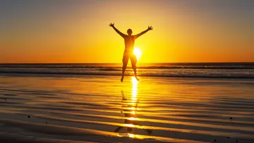 Person, die bei Sonnenuntergang am Strand springt.