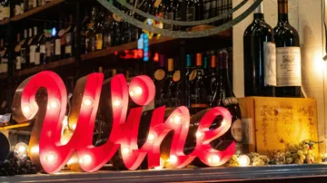 Beleuchtetes Weinschild mit Flaschen im Hintergrund.