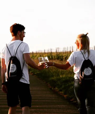 Two people clinking glasses while walking in vineyard.